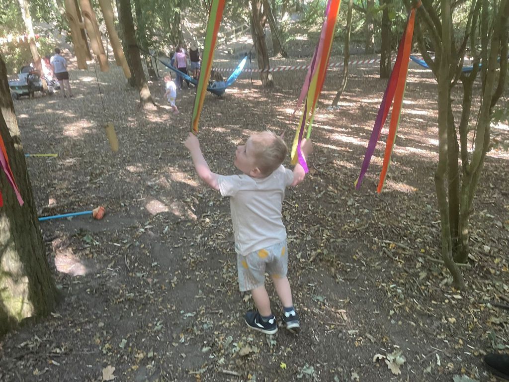 A toddler swinging through ropes attached to trees in the woods
